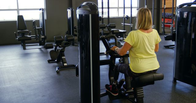 Woman is working out on exercise machine in a modern gym. Useful for fitness marketing, healthy lifestyle promotion, gym environment display, and advertisements for exercise equipment.