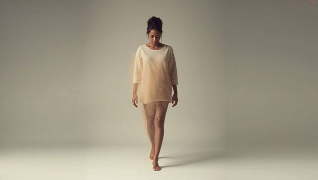 Barefoot woman walking in oversized beige sweater on minimal studio backdrop