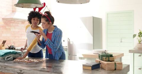 Friends baking holiday cookies in bright farmhouse kitchen capturing treats with smartphone