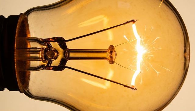 Glowing vintage tungsten filament bulb close-up capturing spark and warm amber glow