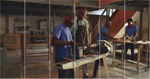 Instructor guiding apprentice shaping spindle on wood lathe in carpentry workshop