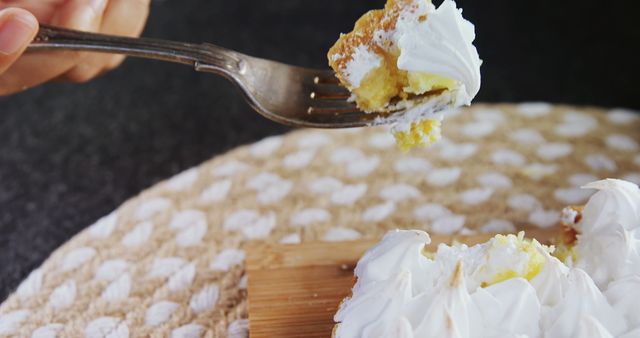 This close-up shows a person's hand holding a fork with a piece of lemon cake. The dessert features rich frosting, making it look indulgent. This kind of imagery is perfect for food blogs, bakery advertisements, recipe sites, or promotional materials for dessert products.