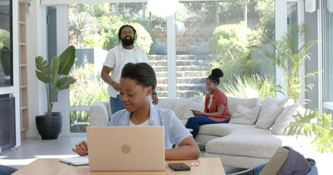 African family working and relaxing in bright modern living room with laptop and phones