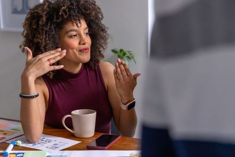 Curly-haired woman discussing creative project over coffee, reviewing worksheets in home office