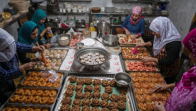 Women in headscarves preparing colorful donuts in busy commercial bakery teamwork