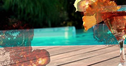 Poolside cocktail with yellow flower and paint-splatter over turquoise water, wood planks