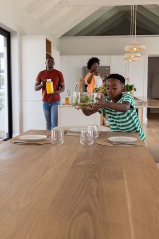 African american family preparing dinner in sunlit open-plan kitchen, boy carrying salad