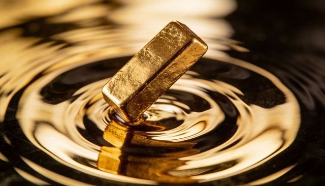 Tilting gold ingot creating concentric ripples in glossy reflective liquid with warm glow