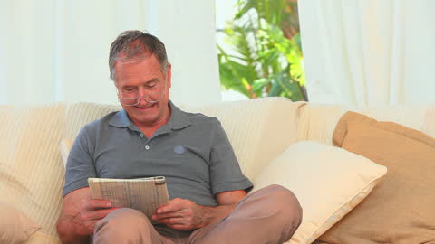 Senior Man Relaxing on Couch Enjoying Newspaper Reading