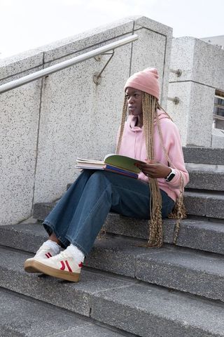 African american student sitting on concrete steps reading notebook on urban campus
