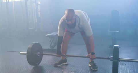 African american man preparing to deadlift heavy barbell in foggy gym strength training