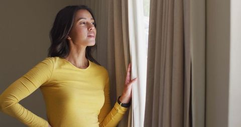 Thoughtful Woman in Yellow Top Looking Out Well-Lit Window