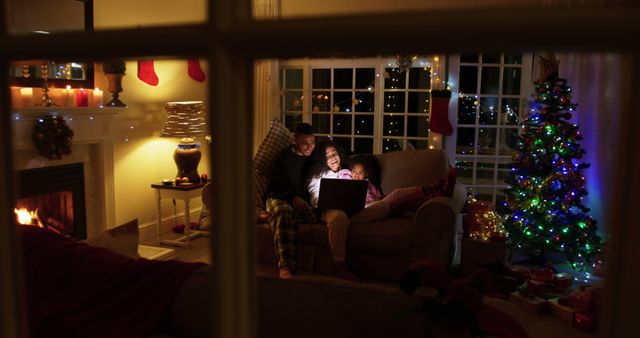 A family sitting on a sofa in a warmly lit living room during Christmas, with decorations set up around the room including a Christmas tree and stockings hanging by the fireplace. This image can be used in promotional materials, holiday greeting cards, online ads, and social media posts to convey a sense of warmth, festivity, togetherness, and the holiday spirit.