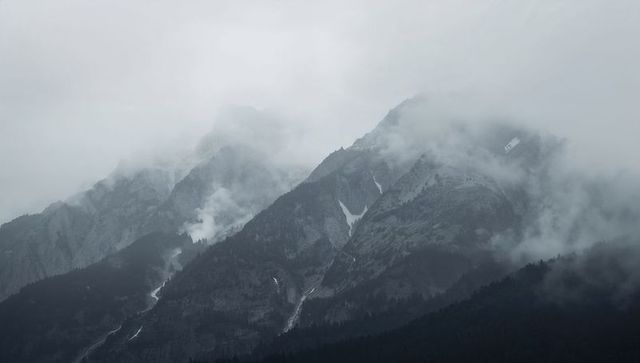 Misty alpine peaks revealing melting snow streaks and rugged ridge silhouettes