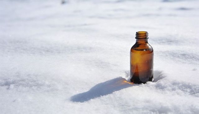 Amber glass bottle standing in snow casting long shadow on bright minimal white background
