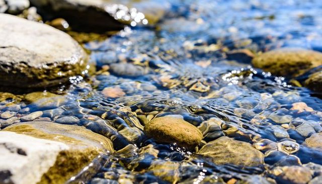 Sunlit creek pebble close-up with glinting water ripples and crystal refractions