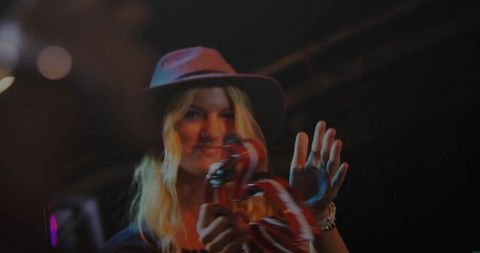 Blonde singer holding tambourine with red ribbons performing on stage under moody spotlight