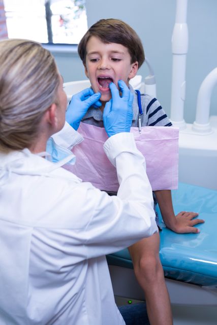 Dentist examining young boy's teeth in a dental clinic. Ideal for use in healthcare, pediatric dentistry, and dental care promotions. Can be used in educational materials about oral hygiene and children's dental health.