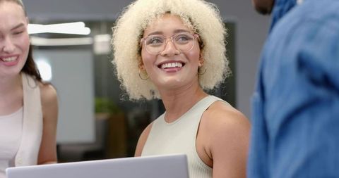 Smiling Asian woman collaborating with colleagues around laptop in modern office