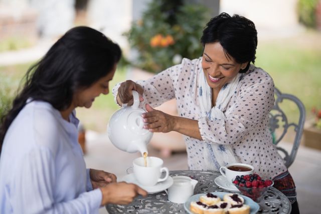 Smiling woman pouring tea in cup for daughter at home