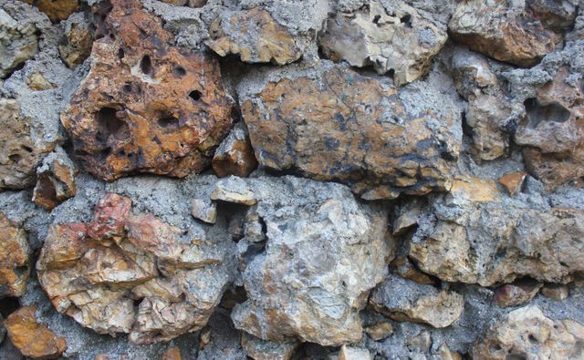 This image showcases a close-up of a rough rock wall with a mix of rusty and weathered stones. The earthy tones and geological textures make it suitable for backgrounds, presentations, or educational materials in geology. It can be used to highlight natural textures and ruggedness in both artistic and scientific contexts.