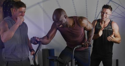 High-intensity air bike workout featuring laughing black man and trainers cheering