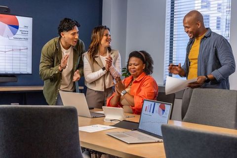 Multiracial team applauding project win in modern conference room with laptops
