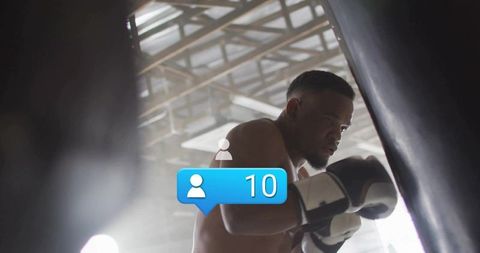 Boxer training on heavy bag, displaying focus and grit, wearing gloves and wraps in industrial gym