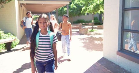 Diverse middle school students walking through sunny school courtyard with backpacks