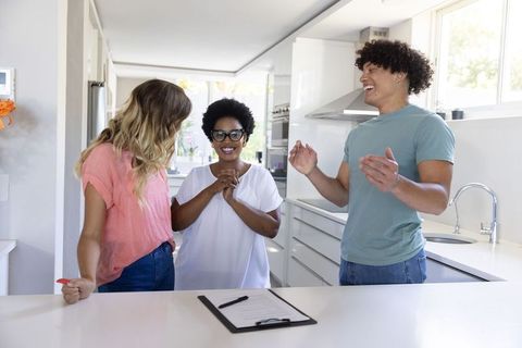 Young buyers celebrating home purchase at modern sunlit kitchen island with agent signing documents