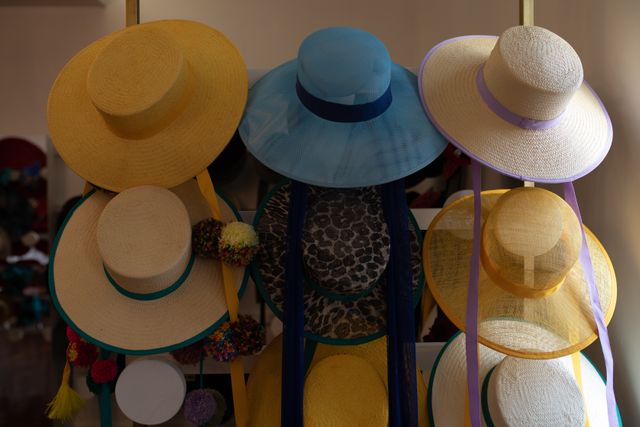 Front view of various styles of hats for women displayed in rows on the white wall of the showroom at a hat makers. 