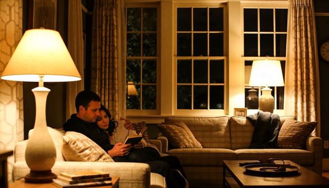 Couple reading and cuddling on cozy living room sofa at night under warm lamp light