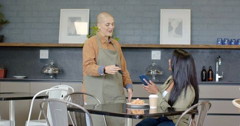 Shaved-head barista offering contactless payment to indian customer in modern coffeehouse