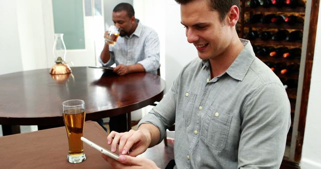 Man enjoying a pint of beer while interacting with a tablet at a cafe. Ideal for illustrating casual and modern settings involving technology, leisure activities, and relaxed environments. Use in advertisements, websites, or articles about modern lifestyles, gadget usage, or cafes.