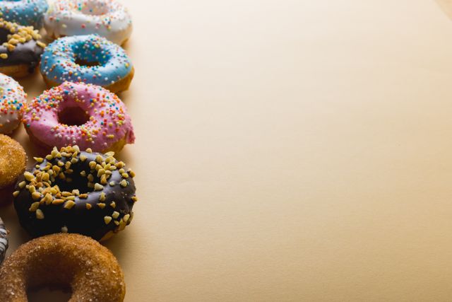 Assorted donuts with colorful sprinkles arranged in a row on a beige background. Ideal for use in advertisements, bakery promotions, food blogs, or social media posts about sweet treats and indulgence.