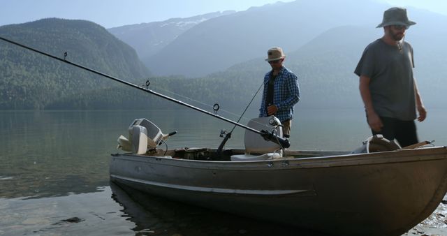 Two men are getting ready to go fishing on a calm mountain lake. They are standing next to an equipped fishing boat, one checking fishing equipment, and the other putting on a hat. This image can be used to illustrate outdoor activities, fishing experiences, nature adventures, peaceful getaways, and recreational hobbies.