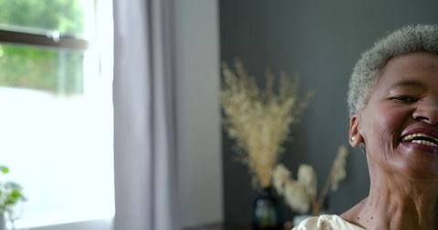 Smiling mature woman turning toward camera by window in cozy minimalist home interior