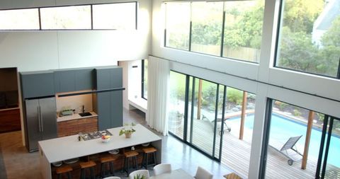 Modern kitchen island anchoring open-plan living with floor-to-ceiling glass opening to pool
