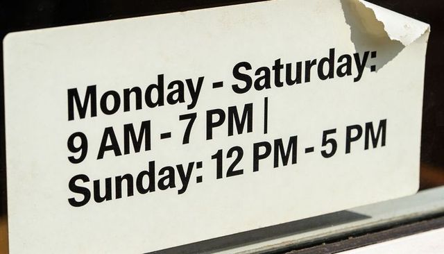 Storefront hours sign showing mon-sat 9 am-7 pm, sun 12 pm-5 pm with peeling corner