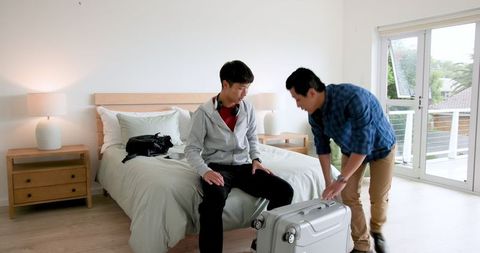 Father and son sharing joyful moment in bedroom with suitcase