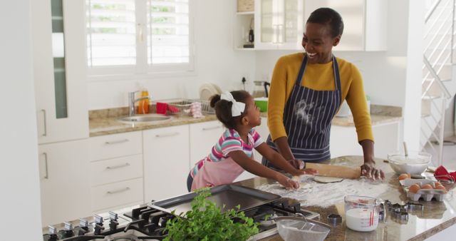 Happy african american mother and daughter wearing aprons having fun while cooking in kitchen. staying at home in self isolation during quarantine lockdown.