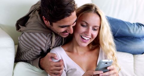 Happy Couple Smiling Together on Couch with Smartphone