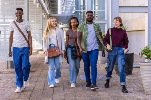 Diverse college students walking together on modern campus walkway carrying casual bags