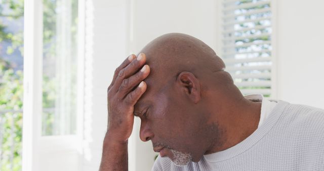 African American man holding head with eyes closed appearing stressed and in pain. Suitable for articles or advertisements on mental health, stress management, healthcare for seniors, headache remedies, and depression awareness.
