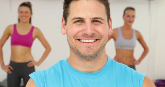 This image shows a smiling fitness instructor leading an exercise class with two women in the background. It is ideal for use in promotional materials for gyms, fitness programs, health and wellness articles, and workout routine guides.