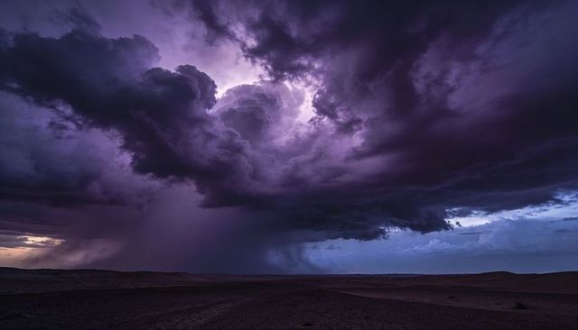 Violet supercell thunderstorm over desert plain releasing rain shaft and illuminated core