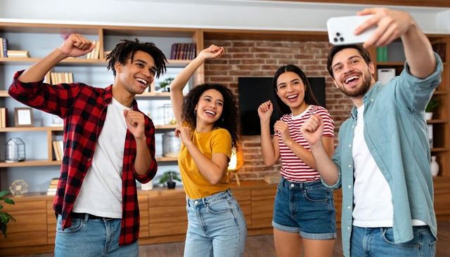 Group of friends taking selfie and dancing in cozy living room celebrating together