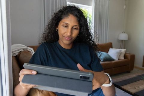 Relaxed african american woman using tablet on leather sofa by window in cozy living room