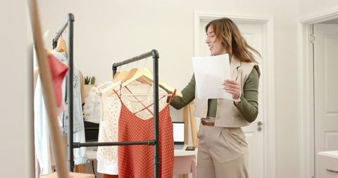 Fashion stylist organizing clothing rack in minimal home studio holding order sheet