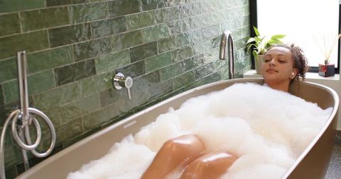 African american woman relaxing in freestanding tub with bubble bath and green tile spa